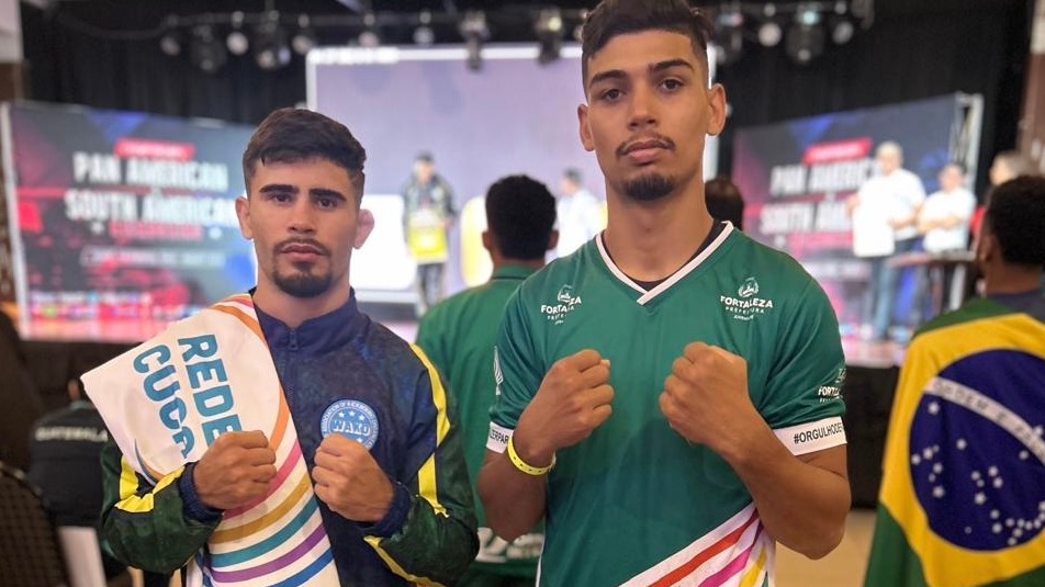 Os atletas Mariano Neto e Mateus Albino posam para a foto, Mariano está com uma bandeira da Rede Cuca pendurada no ombro
